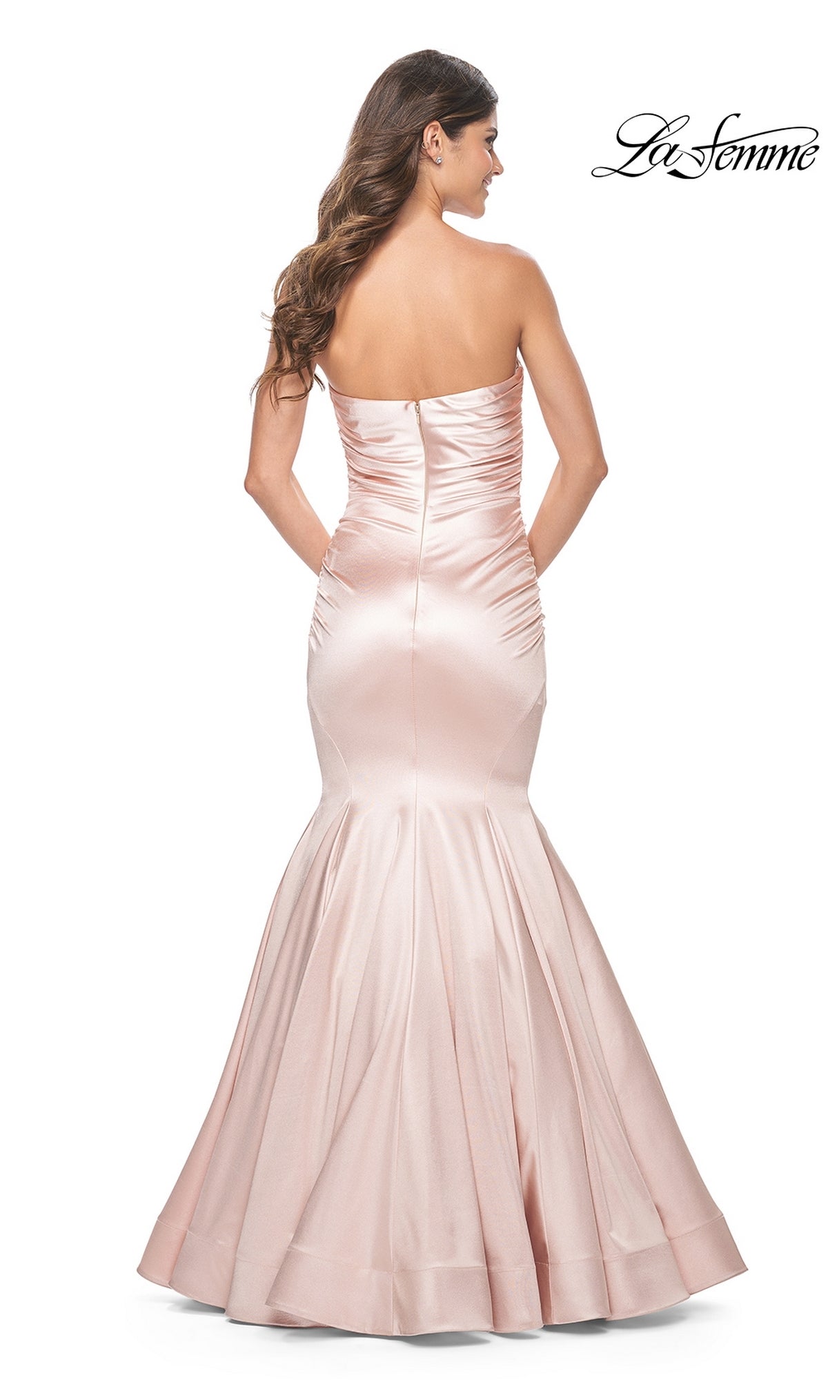 A woman models the La Femme Strapless Long Mermaid Prom Dress 31980 in blush pink satin with ruched detailing, shown from the back against a white background.